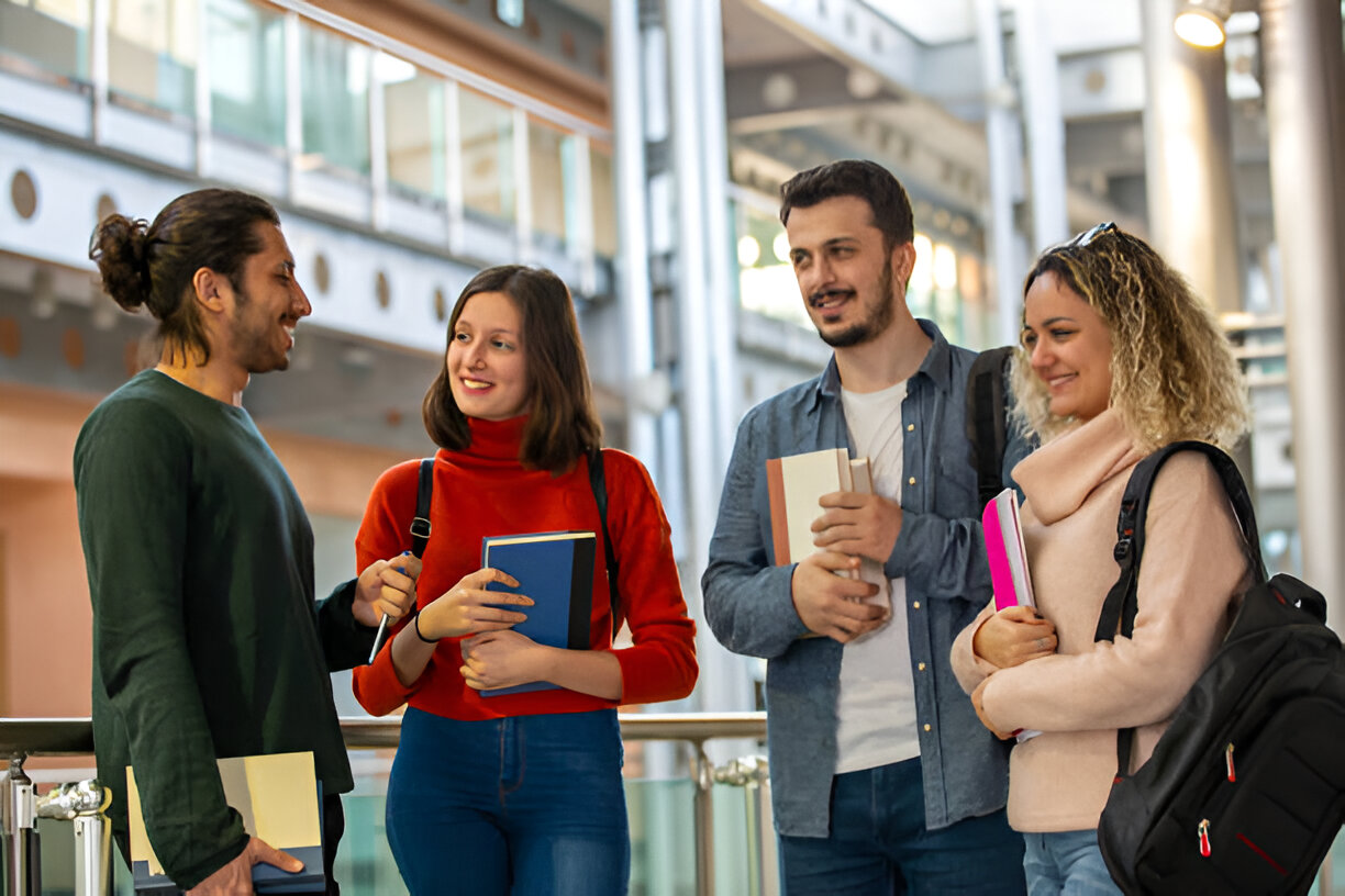 Group of university students chatting and holding books in a modern campus hallway.